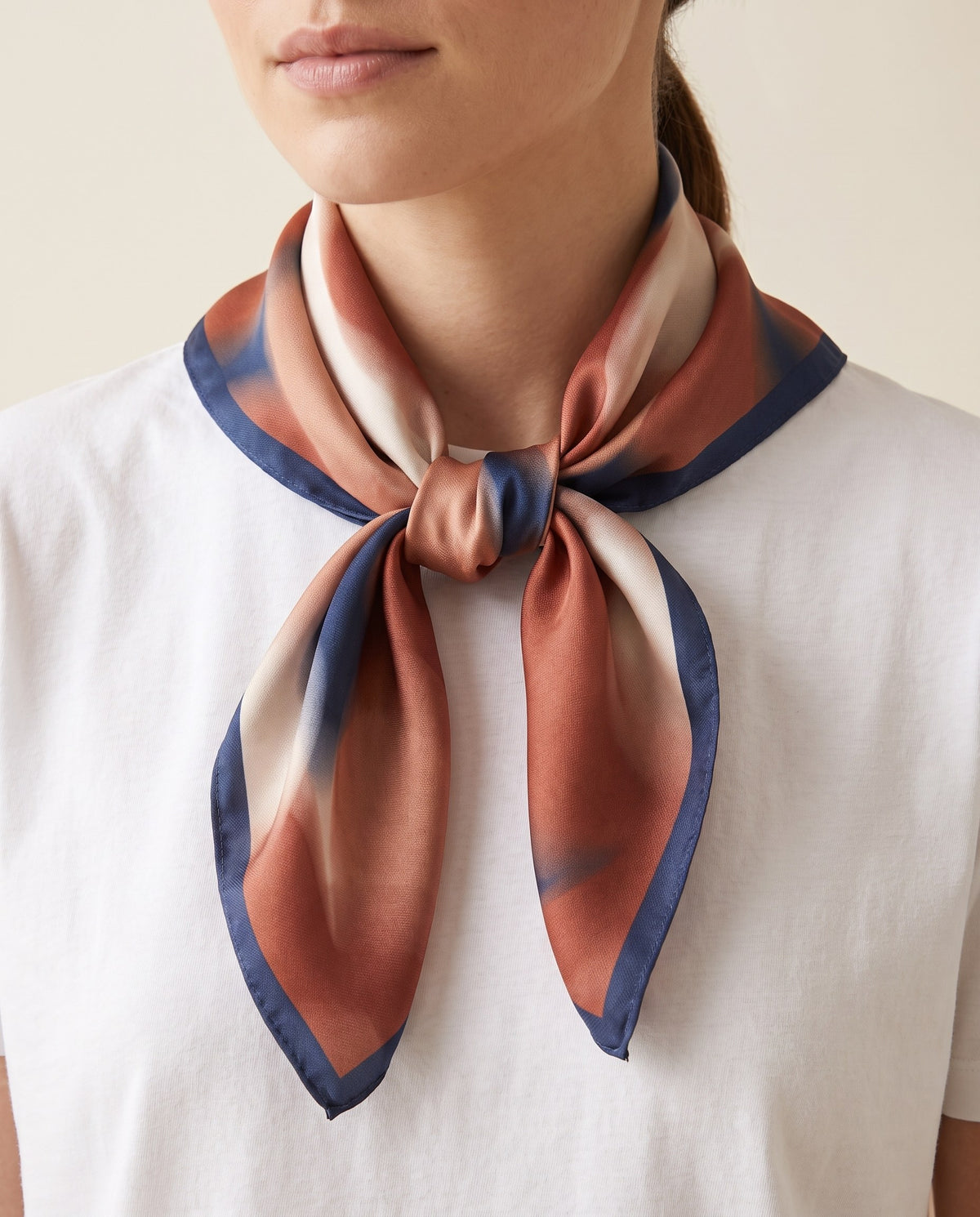 Woman wearing the abstract print square satin scarf tied at the neck over a white top