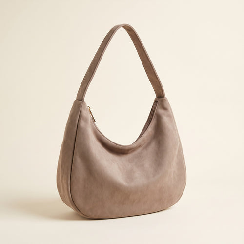 Crescent Hobo Shoulder Bag in taupe faux suede with a wide shoulder strap on an ivory background