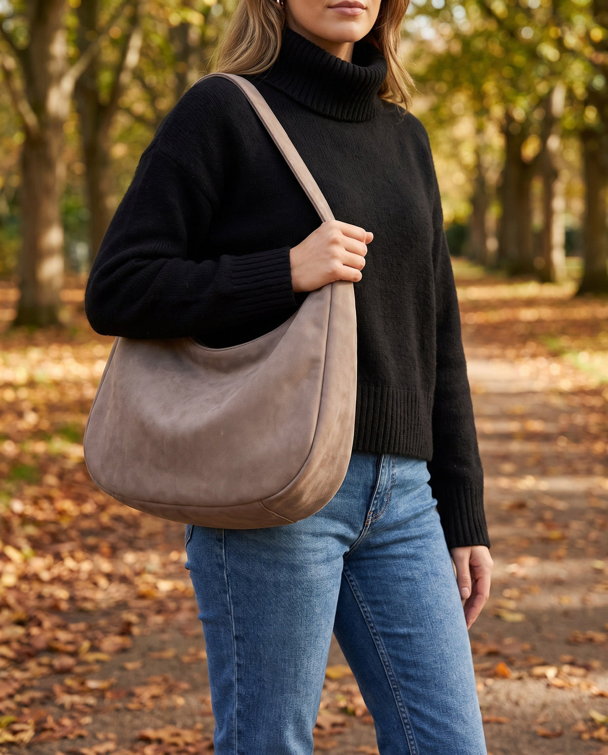 Woman in a black jumper and jeans carrying the taupe Crescent Hobo Shoulder Bag in an autumn park