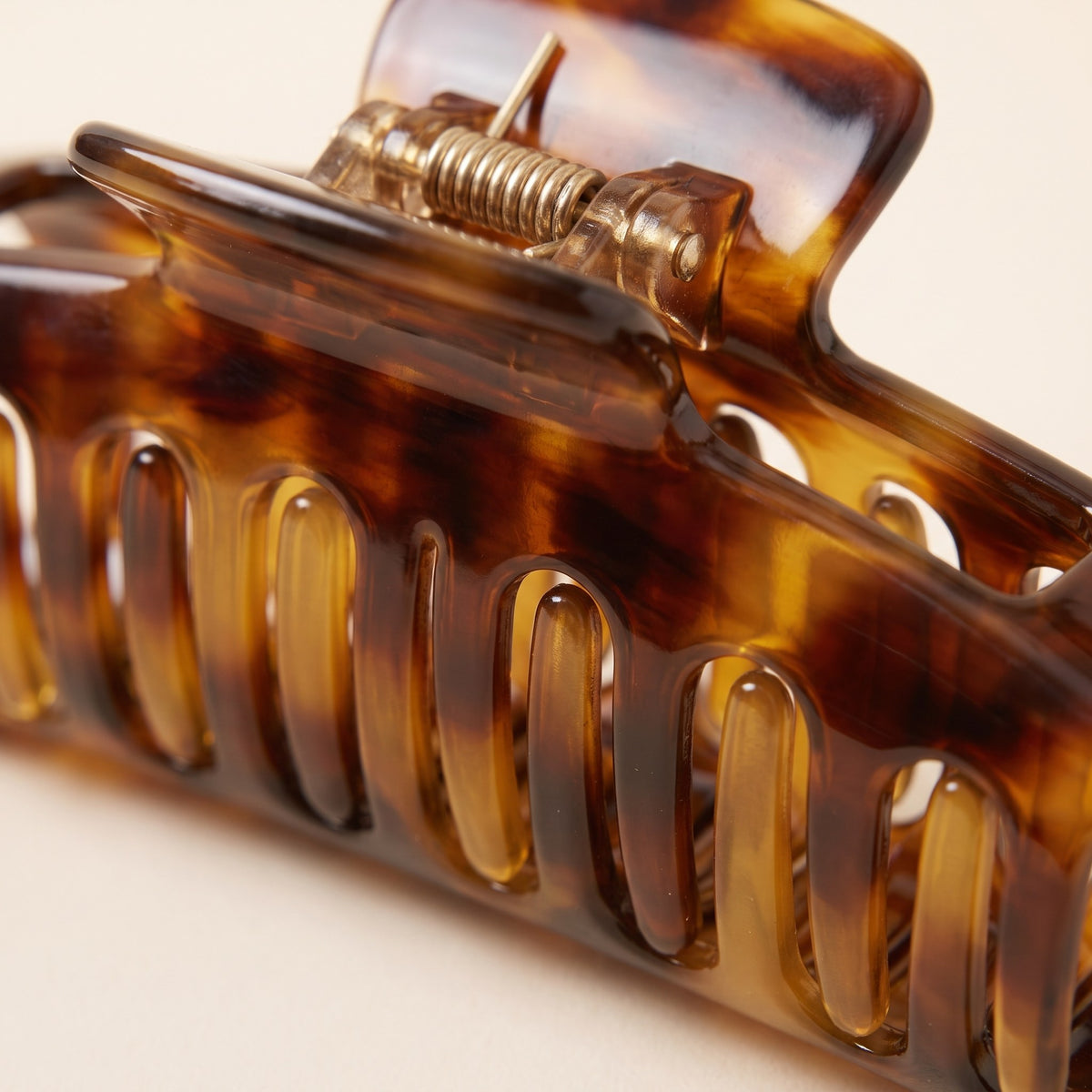 Close-up of the amber tortoiseshell pattern, teeth and spring hinge of the acetate claw clip