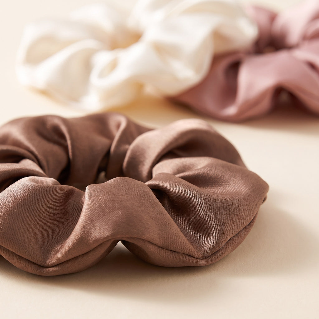 Close-up of the glossy mocha satin scrunchie with the ivory and blush scrunchies behind it
