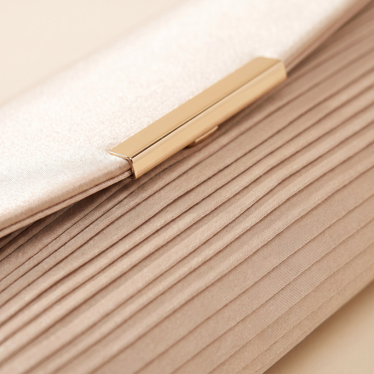 Close-up of the fine satin pleats and the gold-tone bar clasp on the champagne evening clutch