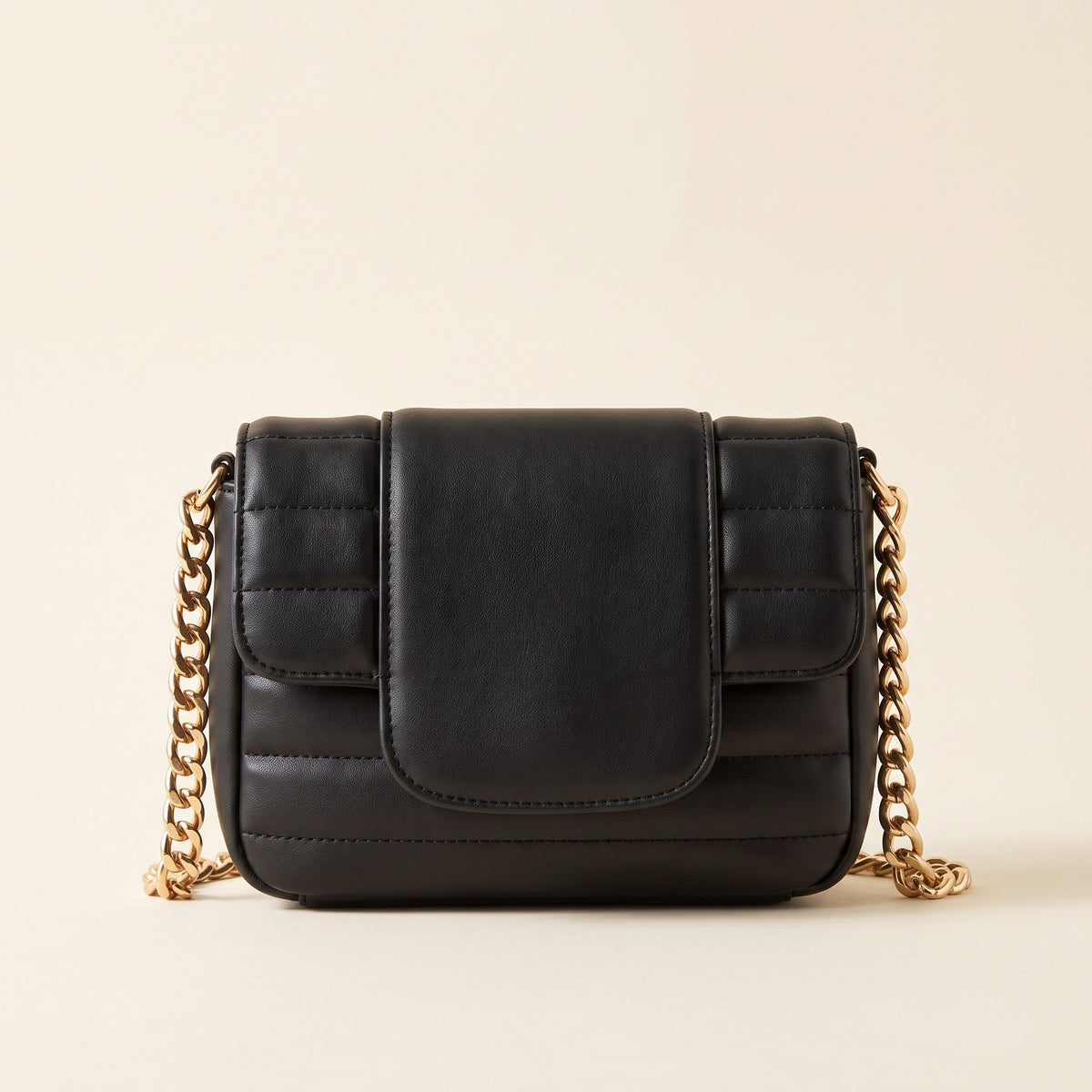 Quilted Chain Crossbody Bag in black channel-quilted faux leather with a chunky gold-tone chain strap on an ivory background