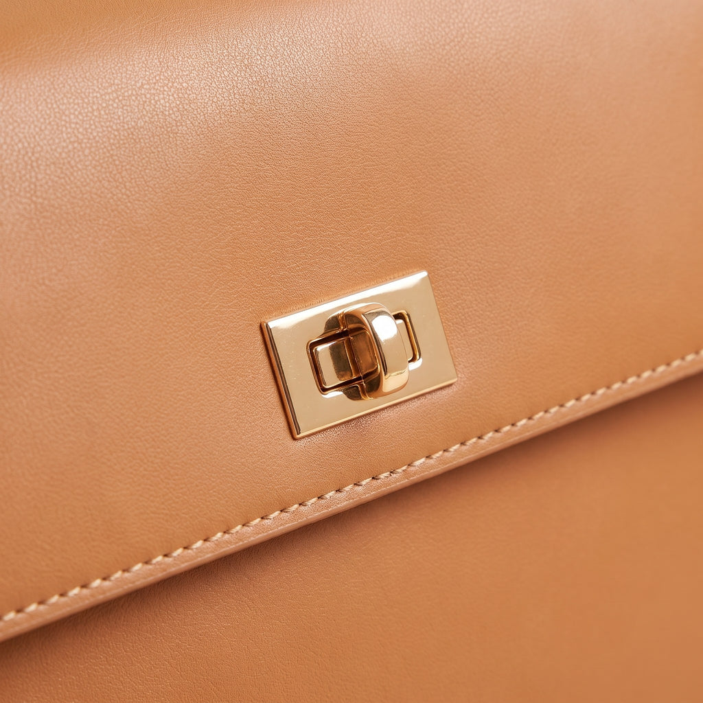 Close-up of the gold-tone turn-lock and edge stitching on the tan faux leather top-handle bag