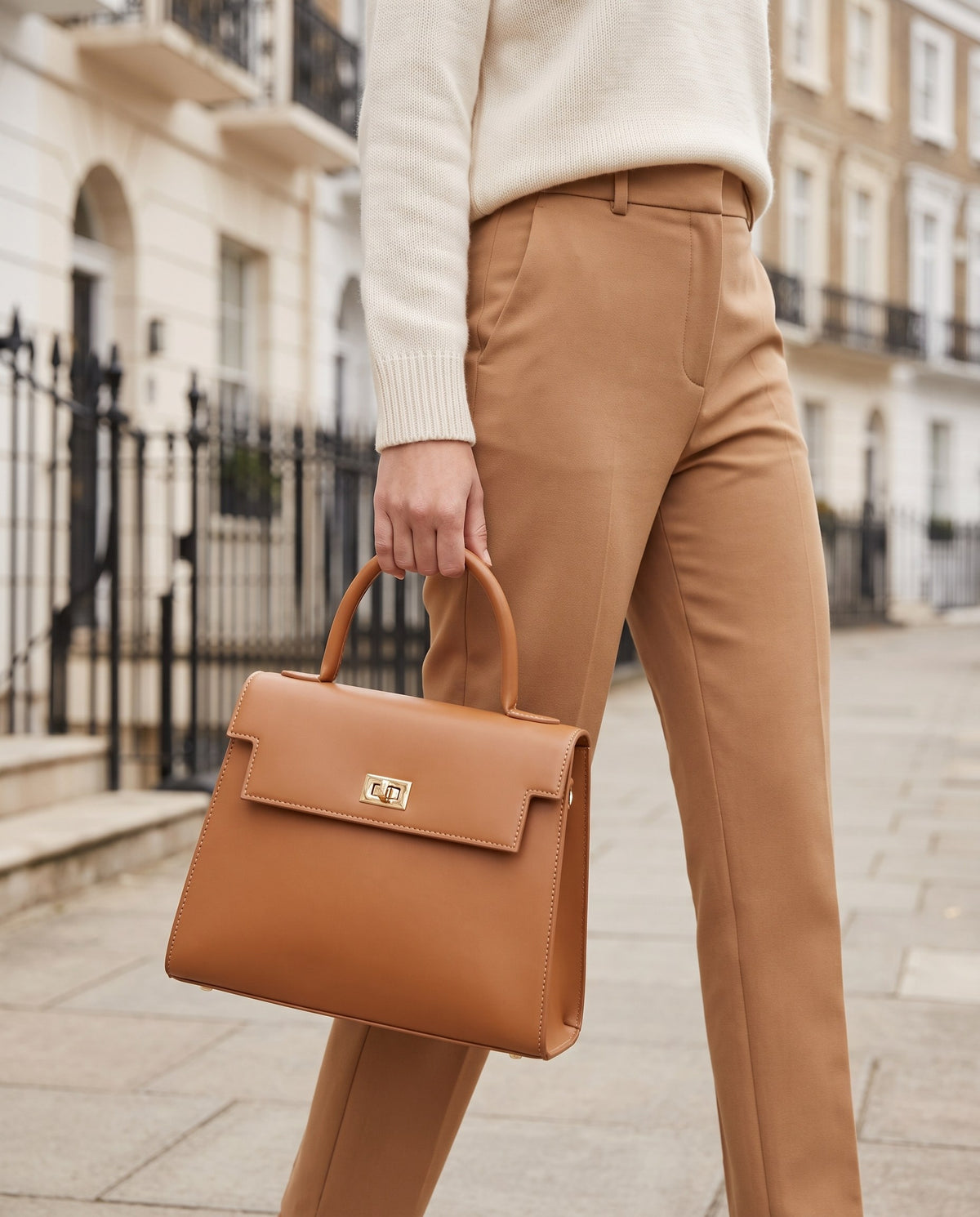 Woman in a cream jumper and camel trousers carrying the tan Structured Top-Handle Bag on a London street