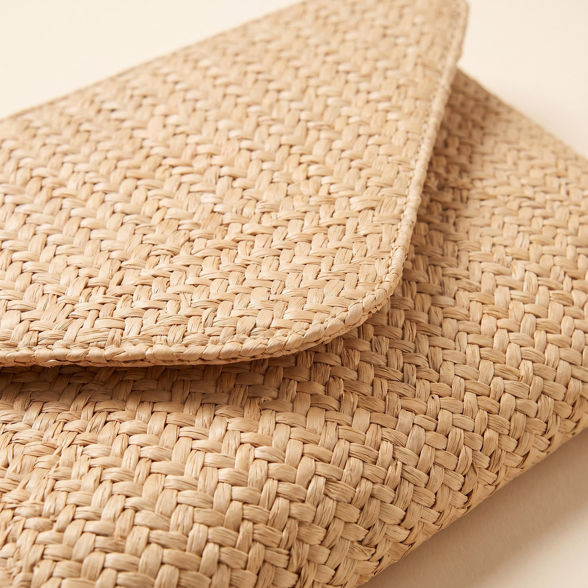 Close-up of the tight basket weave and envelope flap of the natural straw clutch