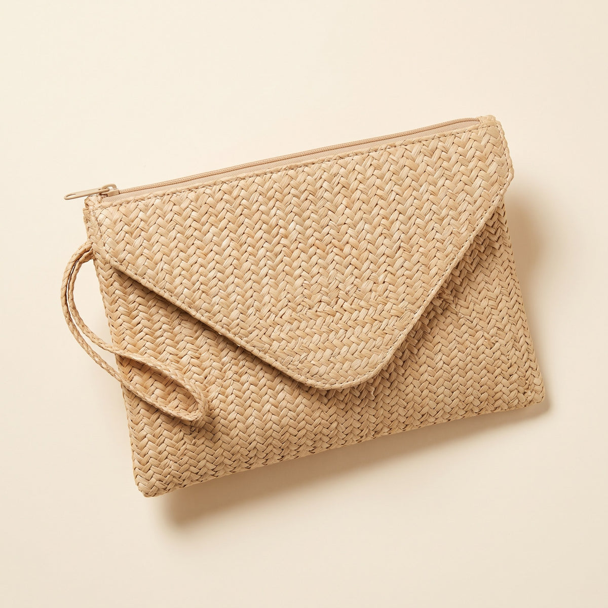 Woven Straw Envelope Clutch in natural beige with zip top and wrist strap on an ivory background