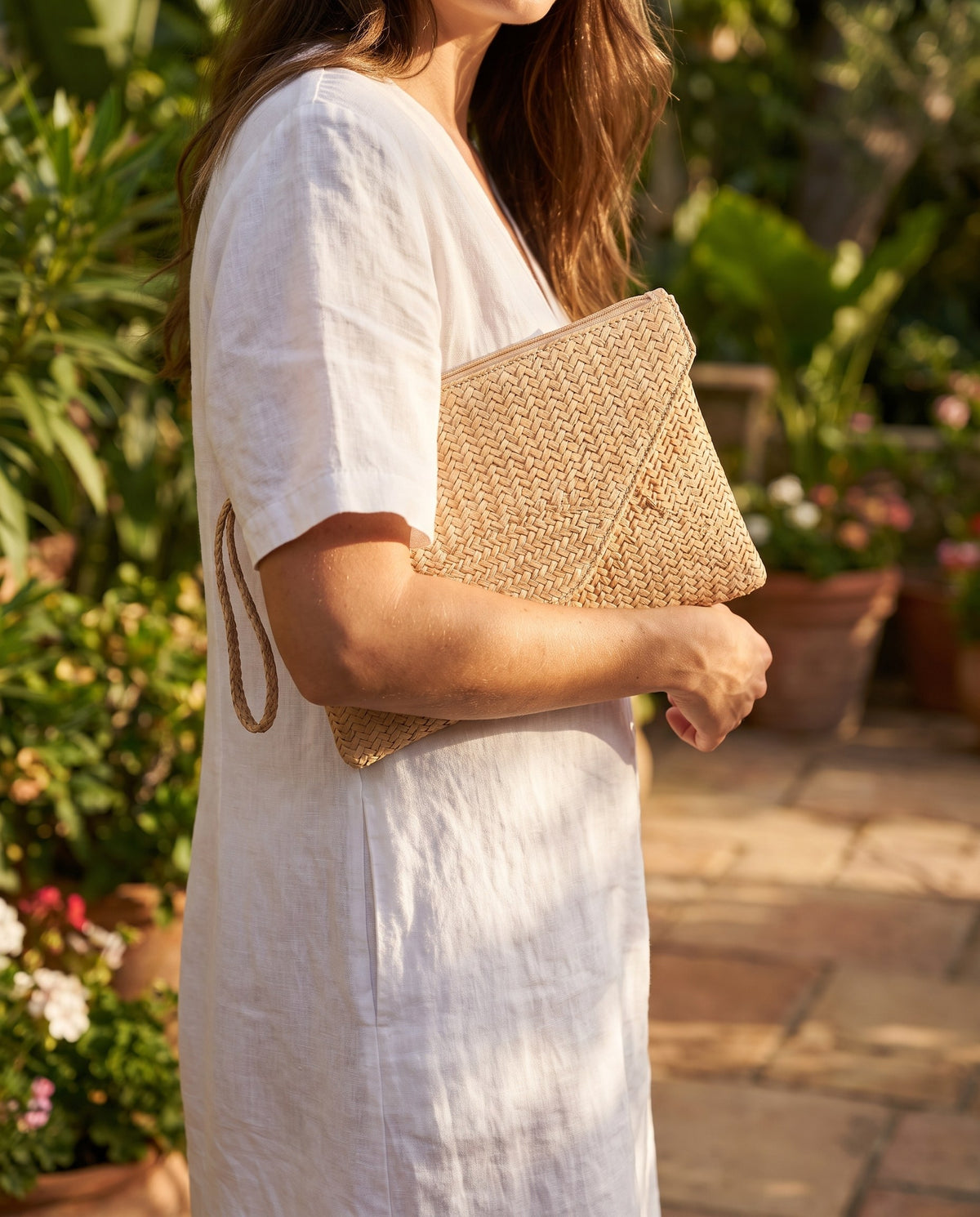 Woman in a white linen dress holding the natural Woven Straw Envelope Clutch in a garden